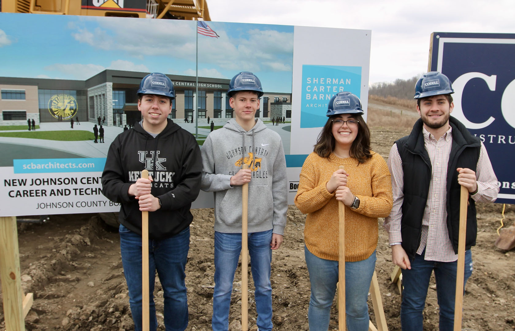 Four students wearing hard hats holding shovels at a groundbreaking ceremony for a new career and technical center.