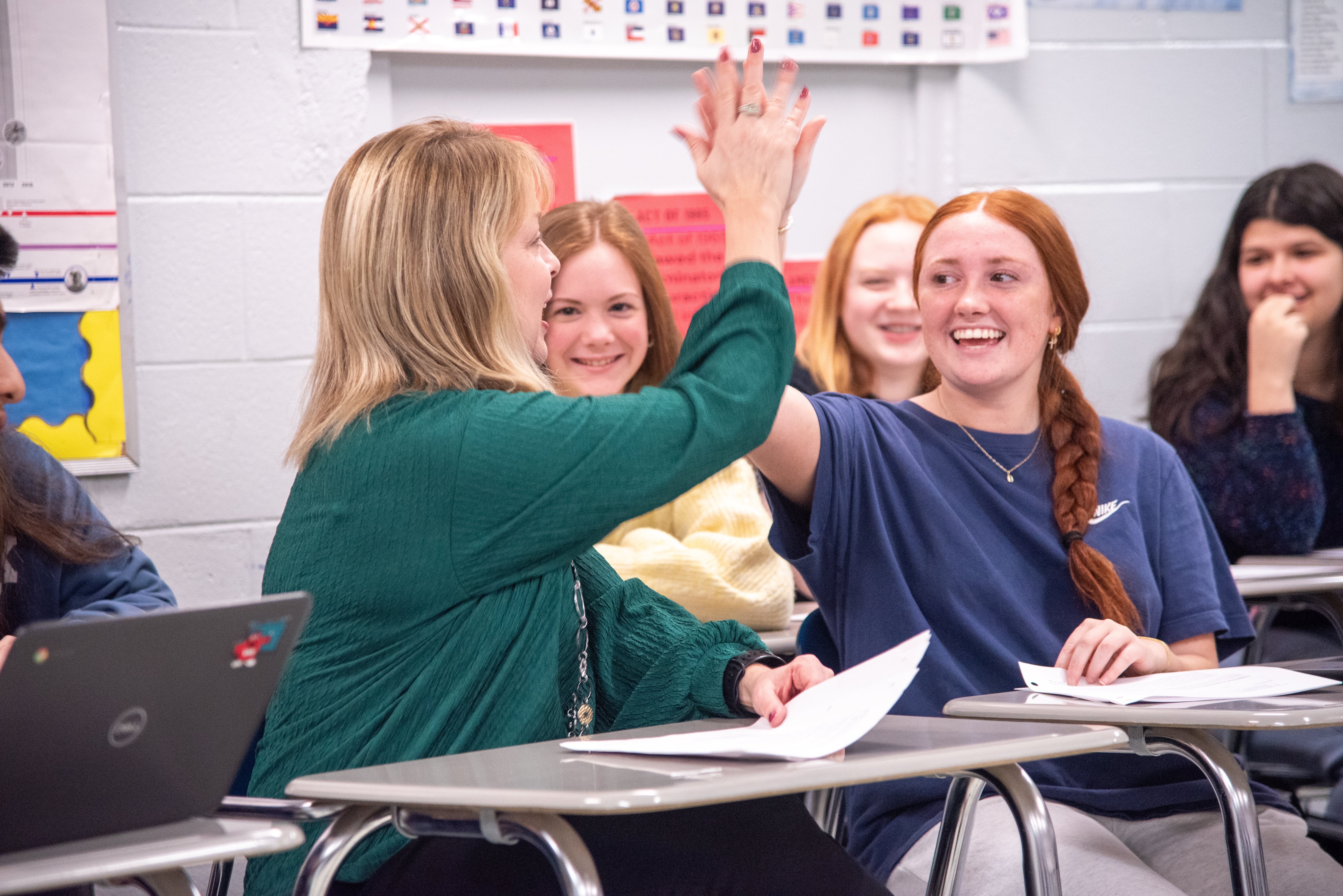 Teacher and student high-five in a classroom while other students smile and watch.