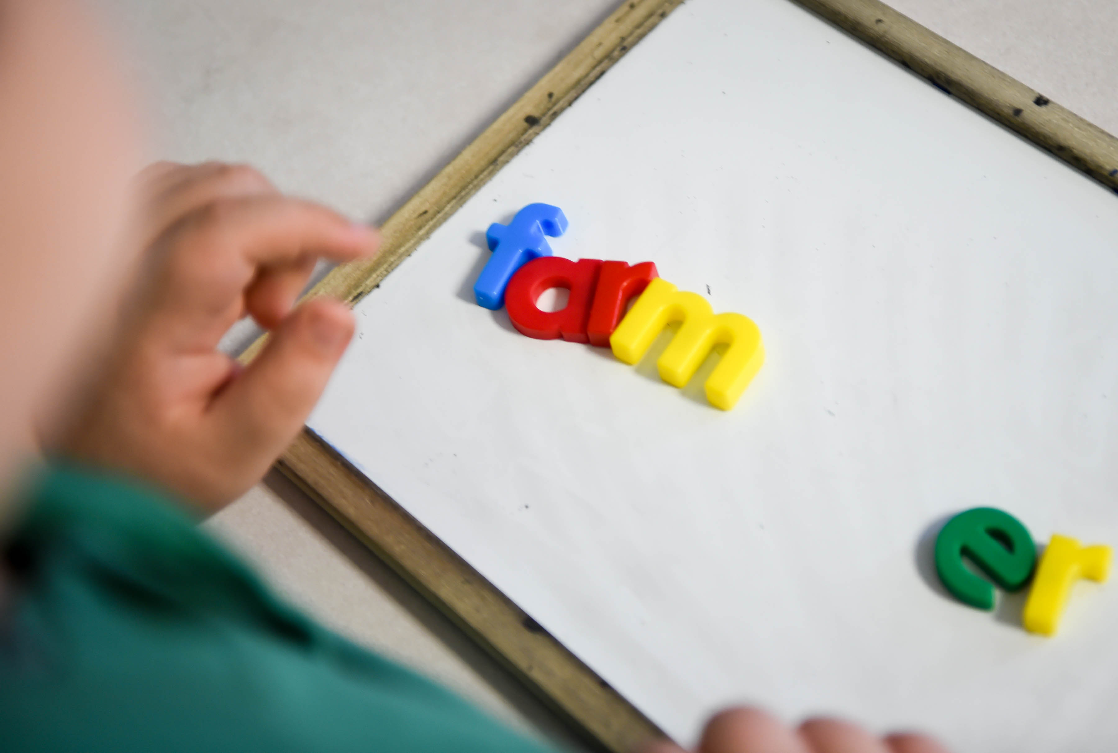 student spelling farmer on a white board with magnetic letters, famer is split into syllables