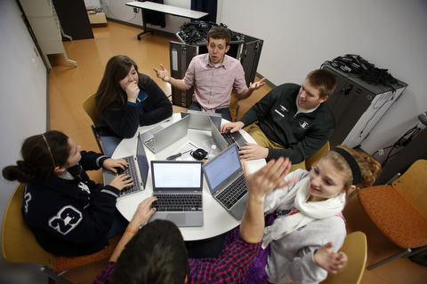 Students sit around a table with computers discussing technology